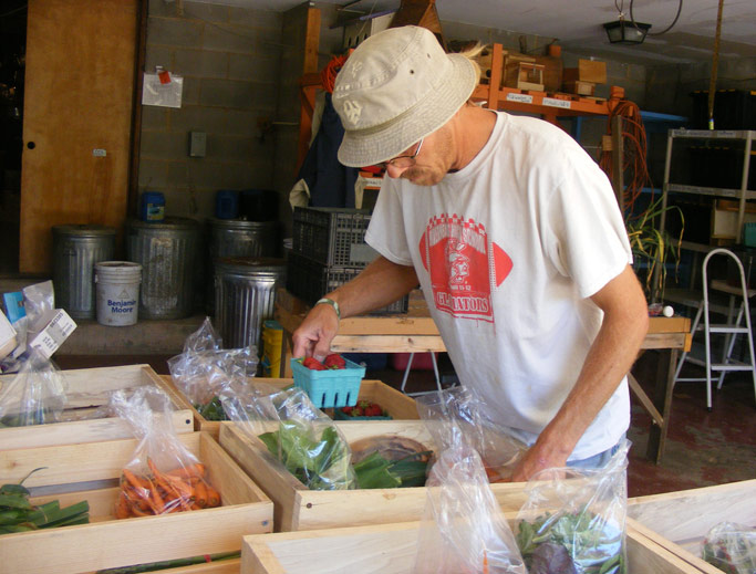 Joel Dollarhite, a tranSender working at OCF, assembles the  contents of a CSA (community supported agriculture) basket.