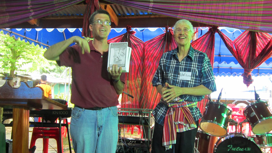 Mark Schoenhals and Richard Showalter introduce Richard Showalter’s book, “Footprints of God,” translated into Thai for the event. Photo by Carol Tobin