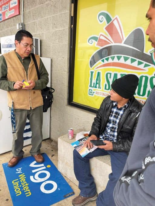 Sergio (à esquerda), membro da Iglesia Shalom, e o pastor Armando Sanchez (à direita) compartilham o evangelho com um homem do lado de fora de uma loja local.